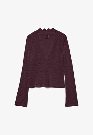 Długa rękaw, głęboko burgundowa koronkowa bluzka z falbaniastym dekoltem w kształcie litery V, lekko skróconym dołem i kwiatowym wzorem na materiale.