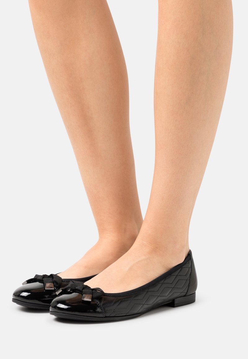Zapatos de ballet negros con una parte superior texturizada, punta redondeada y detalle de lazo. Material brillante con un tacón bajo y un sutil patrón geométrico.