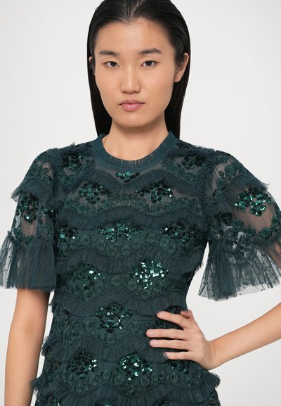 Türkisblaue, mit Pailletten verzierte Bluse mit strukturiertem, schichtigem Design, durchsichtigen Puffärmelchen und geripptem Halsauschnitt. Mit floralen Mustern verziert.