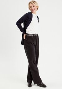 Pantalones de mezclilla negros con corte recto, combinados con una camiseta blanca y un cárdigan azul marino. El conjunto incluye un cinturón negro con ojales de metal.