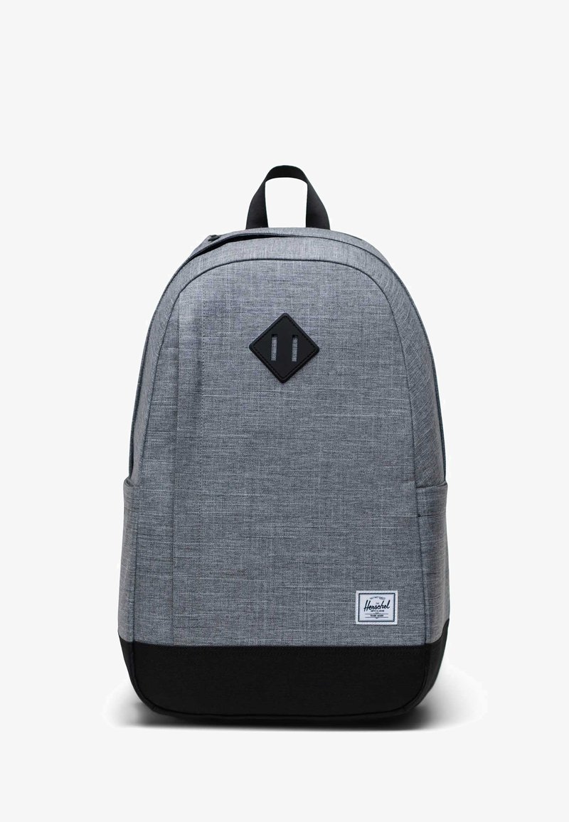 Grijze stoffen rugzak met een gladde textuur, ronde vorm, zwarte onderkant en een ruitvormig patch op de voorkant met twee verticale lijnen.