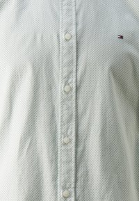 Camicia button-up azzurro chiaro realizzata in un tessuto liscio, caratterizzata da un piccolo motivo geometrico ripetuto e un logo sul lato sinistro del petto.