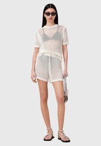 Hvid strikket sæt bestående af top og shorts med et rutemønster; inkluderer korte ærmer og elastisk talje med snørebånd. Sættet bæres med remsandaler og solbriller.