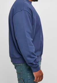 Suéter azul con cuello redondo clásico, mangas largas y puños acanalados. Fabricado en una tela suave con una textura lisa y un corte relajado.
