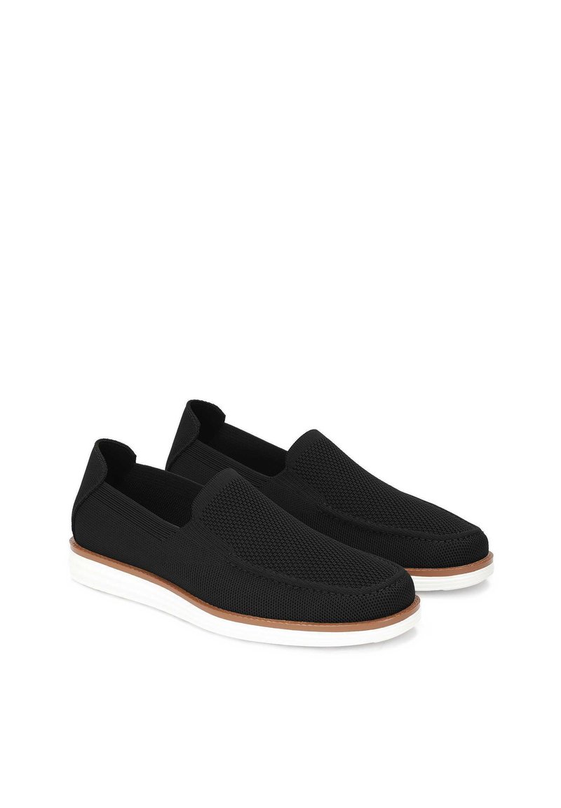 Czarne buty wsuwane wykonane z teksturowanej siateczki, z brązową podeszwą środkową i białą gumową podeszwą dla kontrastu. Minimalistyczny design, bez sznurowadeł.