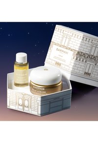 Le coffret de soins Darphin Éclat Sublime comprend une bouteille d'huile claire et dorée ainsi qu'un pot blanc avec une base dorée, le tout présenté dans une boîte illustrée.