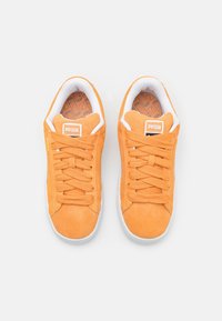 Paire de baskets Puma en daim orange avec semelles et lacets blancs, vue de dessus sur fond blanc.