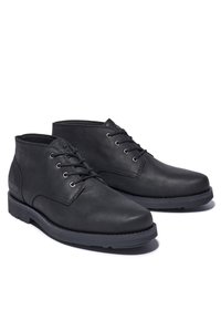 Un paio di stivaletti neri in pelle con lacci, suola in gomma, vista laterale inclinata su sfondo bianco.