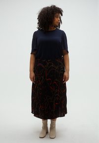 Tengeri kék rövid ujjú felső, fekete plisszírozott szoknyával, mely vörös és arany láncmintával díszített, krémszínű bokacsizmával viselve.