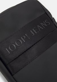 Černé texturované pouzdro na tablet s vyvýšeným logem, hladkým povrchem a zipovým uzávěrem pro bezpečné uložení. Jednoduchý a moderní design.