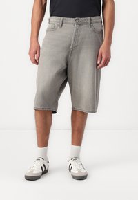 Șorturi din denim gri, cu o croială lejeră, prezentând un design clasic cu cinci buzunare și margini tivite, asortate cu adidași albi și șosete în dungi.