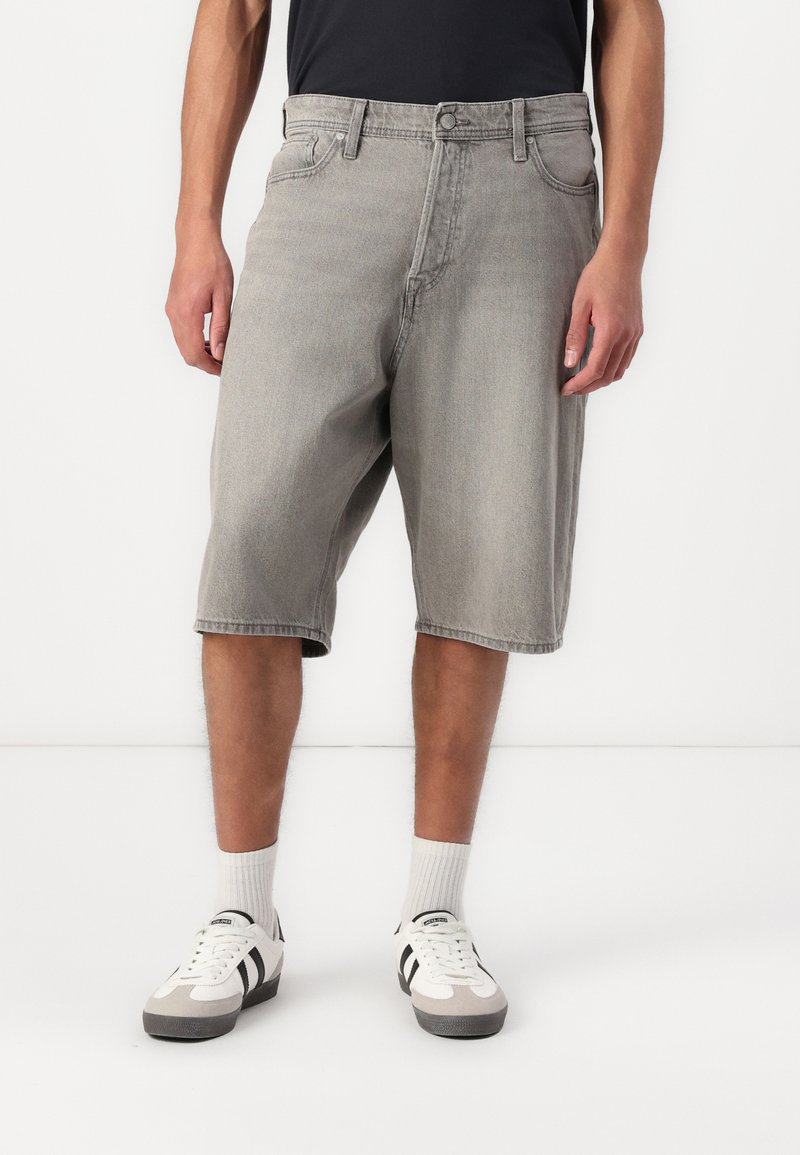 Șorturi din denim gri, cu o croială lejeră, prezentând un design clasic cu cinci buzunare și margini tivite, asortate cu adidași albi și șosete în dungi.