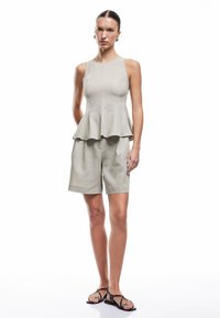Lys grå peplum top med tætsiddende bodice og udfyldt kant, parret med matchende skræddersyede shorts og sorte flade sandaler. Glat tekstur.