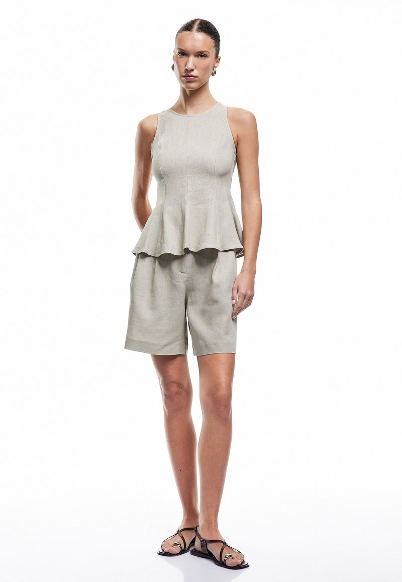Top peplum gris claro con un corpiño ajustado y dobladillo acampanado, combinado con pantalones cortos a medida del mismo color y sandalias planas negras. Textura suave.