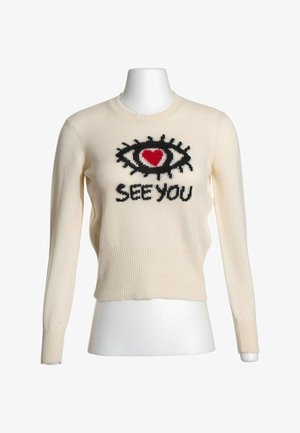 Kremowy sweter z długim rękawem z czarnym okiem i czerwonym sercem nad słowami "SEE YOU" na przodzie, prezentowany na białym manekinie.