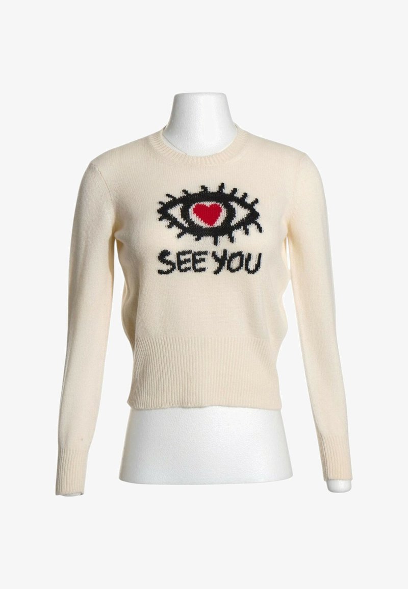 Pull crème à manches longues avec un motif œil noir et cœur rouge au-dessus des mots "SEE YOU" sur le devant, affiché sur un mannequin blanc.