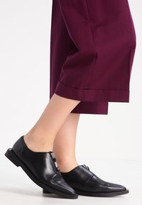 Zwarte leren schoenen met een spitse neus, voorzien van een zijrits. Draag ze met bordeauxrode, cropped broeken die een slank ontwerp laten zien.