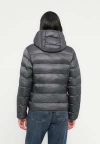 Γκρι φουσκωτό μπουφάν με αποσπώμενη κουκούλα, με οριζόντιες ραμμένες ενότητες και λεία, λαμπερή επιφάνεια. Συνδυασμένο με τζιν.