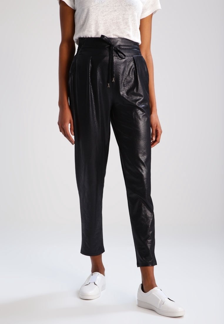 Pantalon noir taille haute avec une finition texturée et brillante, doté d'une taille à cordon. Associé à des baskets blanches pour un look décontracté.