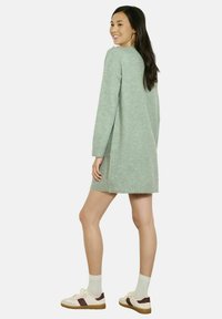 Svetlozelené pletené šaty s dlhým rukávom a lemom nad polovicou stehna. Kombinované s krémovými teniskami a svetlými ponožkami.