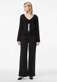 Svart stickad kofta med V-ringning, öppen fram och långa ärmar. Tillsammans med högmidjade svarta vida jeans och spetsiga svarta klackar.