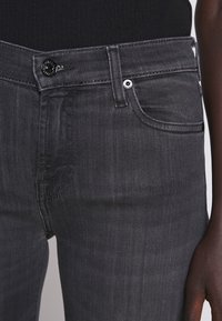 Jeans de mezclilla gris oscuro con una textura suave, que cuentan con un cierre de botón y cremallera, bolsillos frontales y detalles de costura sutiles.