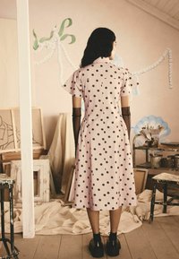 Vestido rosa con lunares, de mangas cortas, largo hasta la rodilla y con pliegues en la espalda. La modelo lleva botas negras hasta el tobillo y guantes negros transparentes.