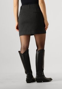 Grauer Rock mit maßgeschneidertem Design, Gesäßtaschen, kombiniert mit knielangen schwarzen Lederstiefeln mit spitzer Zehe und leichtem Absatz.