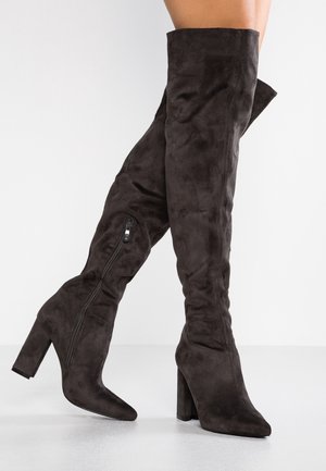 Thigh-high black suede boots with block heels and side zippers worn, shown against a plain white background.