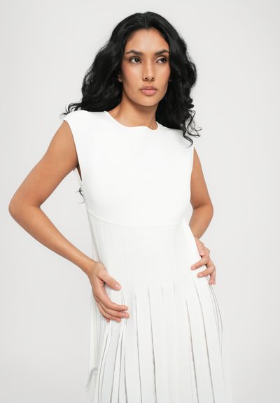 White sleeveless dress with a ribbed bodice and pleated skirt featuring metallic accents. Smooth texture and fitted design.