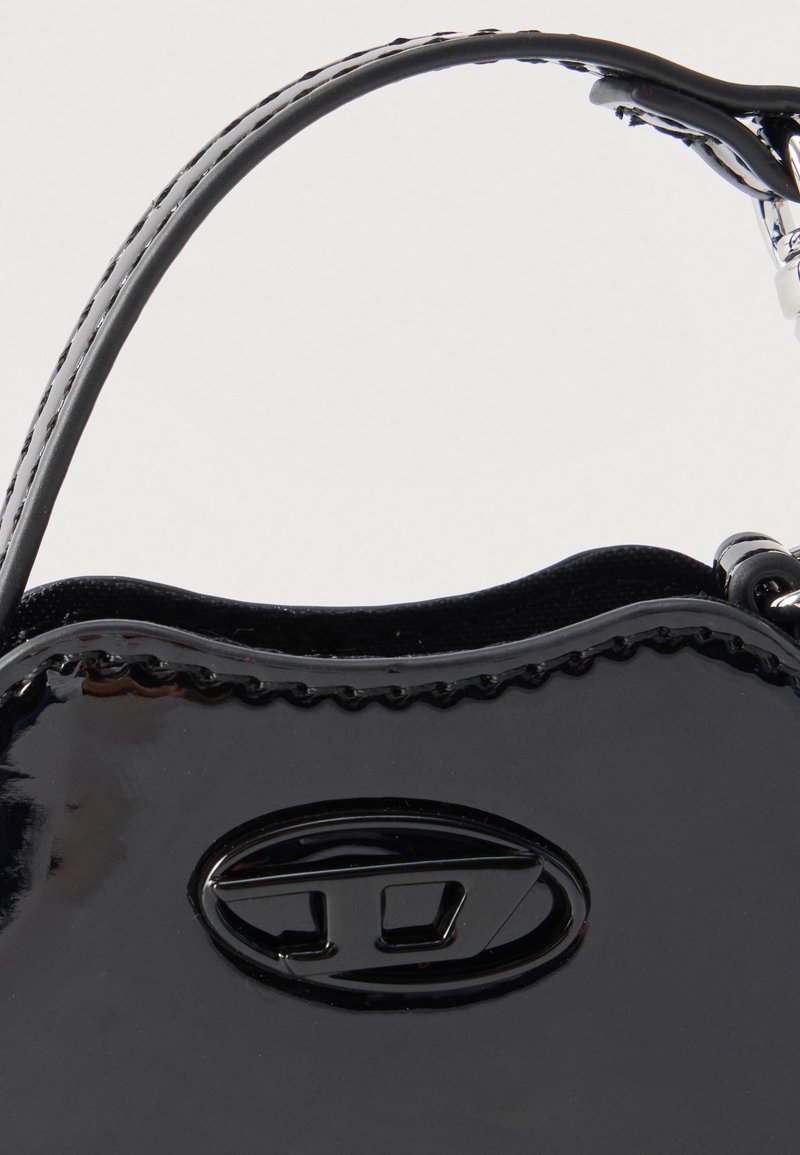 Bolso de mano de charol negro con bordes ondulados, cierre ovalado y asas dobles cortas sobre un fondo liso.