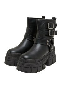 Schwarze Stiefeletten aus Kunstleder mit dicken Plateausohlen, seitlichen Schnallen und strukturierten Gummisohlen. Auffällige hochglänzende Oberfläche.