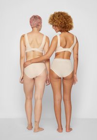 Sostenes de color nude con tirantes anchos y cierres de gancho, combinados con braguitas de cintura alta a juego, presentan una textura suave y un diseño minimalista.