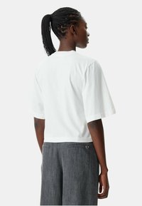 Wit t-shirt met korte mouwen van katoen, met een ronde halslijn. Het model draagt grijze broek met een hartvormige zakdetail.