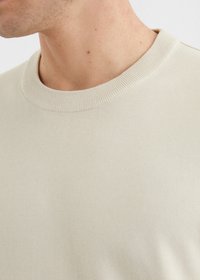 Pull en beige clair à col rond, présentant un col côtelé, une texture douce et un tissu lisse, avec des détails de couture minimes.