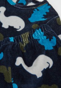Ensemble en velours bleu marine avec des silhouettes blanches de dinosaures et de baleines, agrémenté d'accents bleu clair et vert olive. Taille élastiquée.