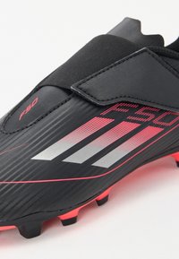 Schwarzer Fußballschuh mit silbernen und roten Streifen, strukturiertem Obermaterial, elastischem Band und pinken Akzenten an der Sohle. Entwickelt für Agilität und Traktion.