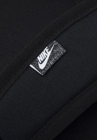 Černá tkanina s texturou, na které je umístěna tkaná cedulka s logem Nike, na poskvrněném černobílém pozadí, vedle hladkého černého okraje.