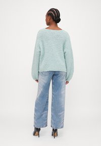 Mintgrön stickad tröja med vida ärmar, kombinerad med ljusblå jeans med en subtil glans och svarta klackskor.