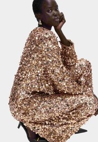Pailletkjole i rose gold, med afslappet pasform, lange ærmer og rund halsudskæring. Stoffet er dækket af små, skinnende runde pailletter.