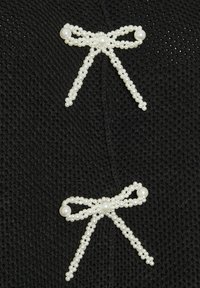 Svart texturerad tyg med två vita pärlbroderade rosetter, var och en med en central pärla och ordnade symmetriskt.