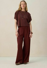 Ensemble deux pièces bordeaux comprenant un top court et un pantalon à jambes larges. Tissu lisse, coupe décontractée, accessoirisé avec des colliers empilés et des bracelets.