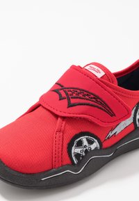 Rode stoffen schoen met een klittenbandsluiting, voorzien van een geborduurd ontwerp van een auto op de zijkant. Rubberen zool, textuurmateriaal en zwarte accenten.