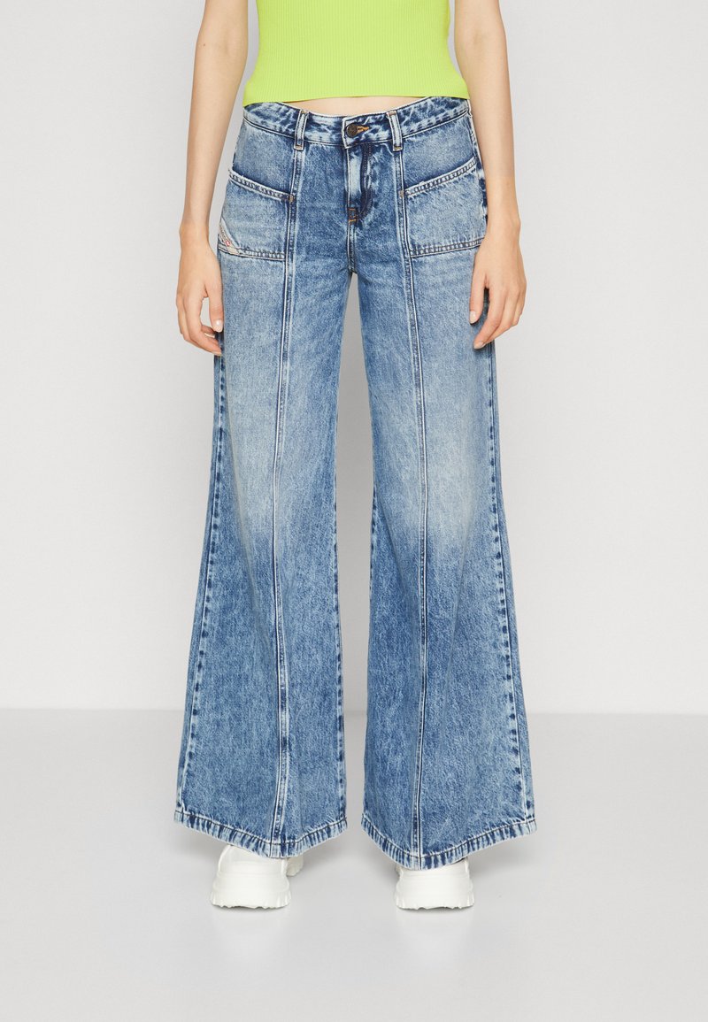 Wide-leg blue denim jeans with a faded wash, featuring front pockets and a drawstring waistband. Textured fabric with a casual design.