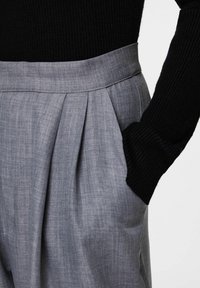 Szare plisowane spodnie z wysokim, usztywnionym stanem, wykonane z teksturowanej tkaniny, zestawione z czarną, prążkowaną bluzką z długim rękawem.