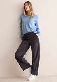 Un pull à manches longues bleu clair associé à un pantalon large noir avec une taille élastique et des poches latérales, porté avec des baskets blanches.