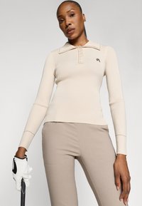 Beige pitkähihainen neulepolo, jossa on muotoiltu kaulus ja nappilista. Teksturoitu ribbikangas ja brodeerattu logo.