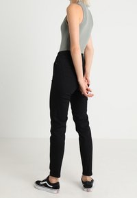 Tilpasset grå ærmeløs bodysuit parret med sorte tapered jeans og sorte sneakers. Jeansene har sidelommer og en glat tekstur.