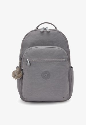 Grijze Kipling rugzak met een voorste ritszak, zijzakken, handvat aan de bovenkant en een klein pluche aapjes sleutelhanger eraan bevestigd.