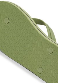 Semelle en caoutchouc vert de tongs avec un motif hexagonal texturé, portant une indication de taille et des détails de logo le long du bord.